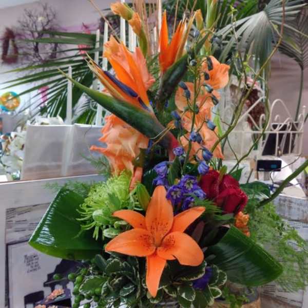 Tall tropical bouquet with orange lilies and purple accents in a glass vase