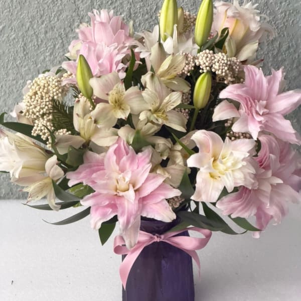 Pink and white lilies arranged in a purple vase with a pink ribbon