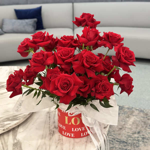 Red roses arranged in a round gift box with a white ribbon.