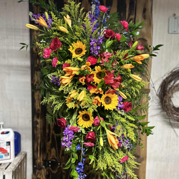 Tall standing spray of sunflowers, orange lilies, and bright mixed flowers on a metal easel.