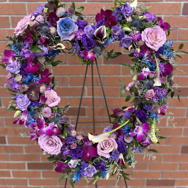 Heart-shaped floral wreath with purple, pink, and blue flowers on a stand