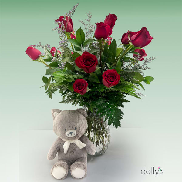 Red roses in a glass vase with a gray teddy bear in front
