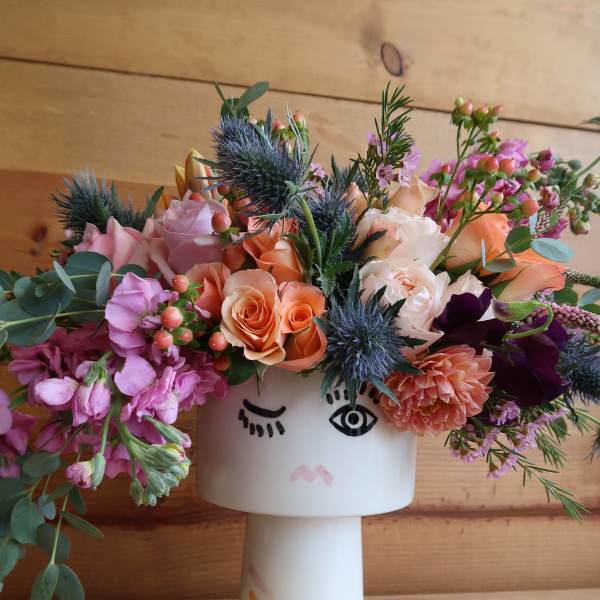 Mixed bouquet in a white face vase with pink, peach, and purple flowers