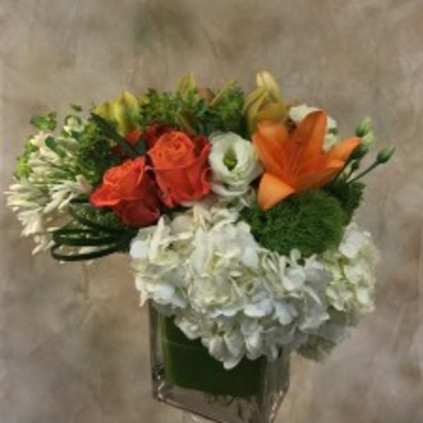 Bouquet of orange and red roses with white blooms in a square glass vase