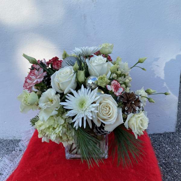 White roses and daisies in a clear vase with pinecones and silver ornaments