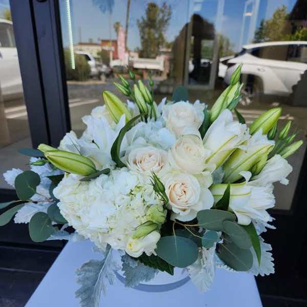 Low arrangement of white lilies, cream roses, and hydrangea in a round white vase