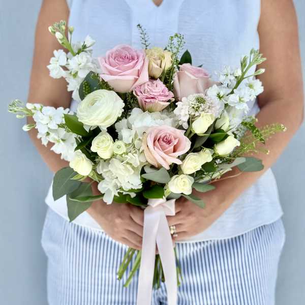 Handheld bouquet of pink and white roses with white blooms and ribbon