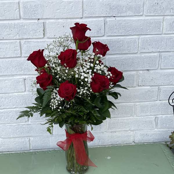 Red roses in a clear glass vase with baby's breath and a red ribbon