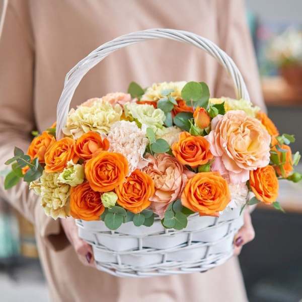 Basket of orange and peach roses with pale carnations