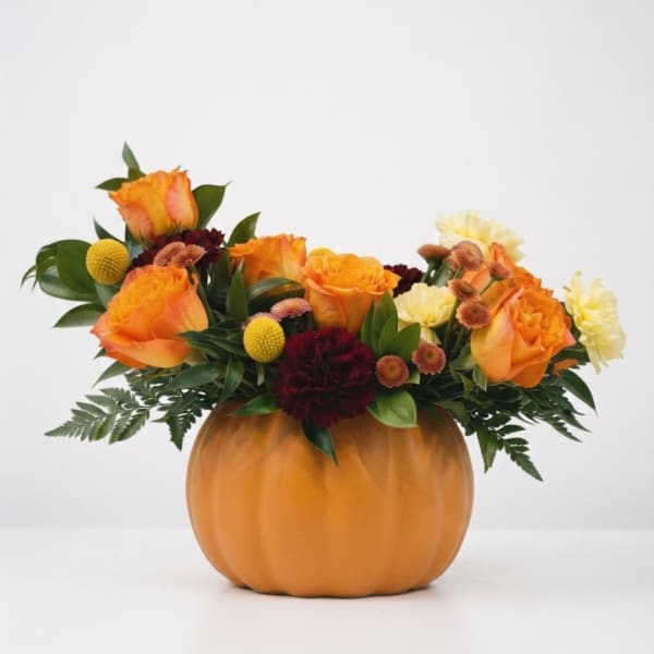 Orange roses and mixed flowers arranged in a pumpkin-shaped vase