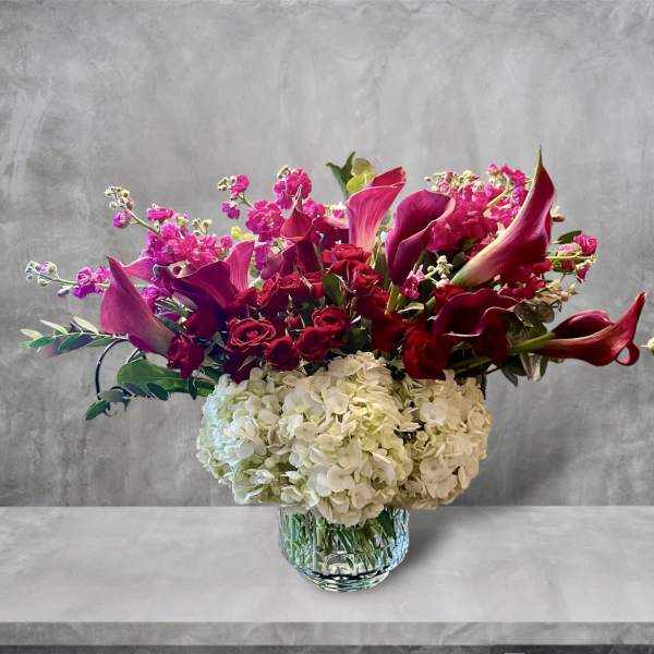 Bouquet of pink calla lilies, red roses, and white hydrangeas in a glass vase