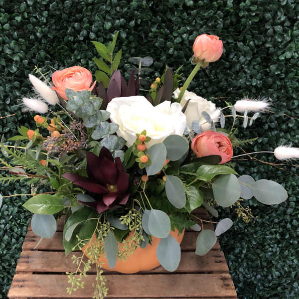 Mixed floral arrangement in an orange container with coral and white blooms