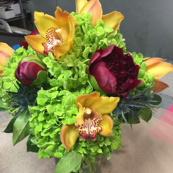 Bouquet of green hydrangeas with yellow orchids and burgundy peonies in a glass vase