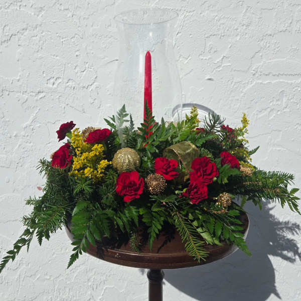 Red carnations and yellow filler in a glass hurricane vase with a red candle