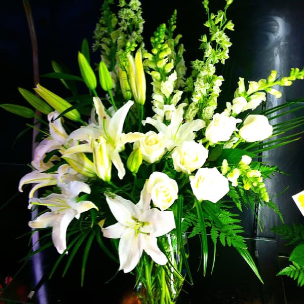 Tall arrangement of white lilies, roses, and snapdragons in a clear glass vase