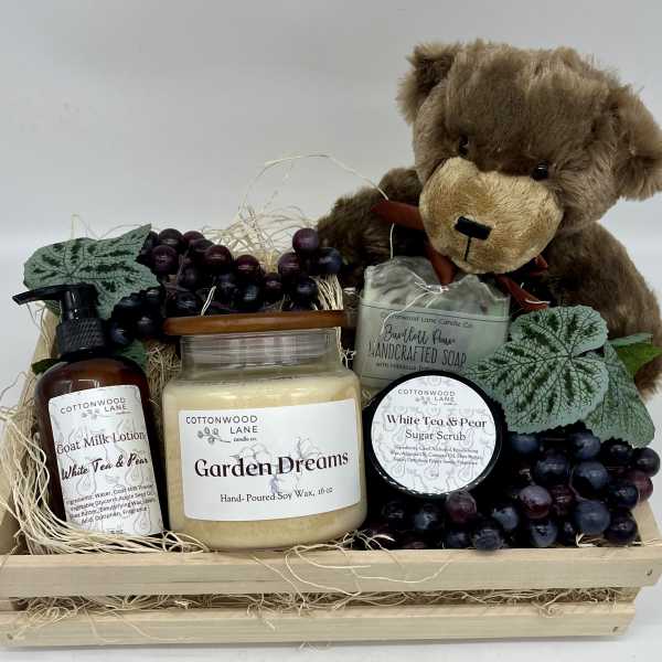 Gift basket with a teddy bear, candles, soap, lotion, scrub, and faux grapes