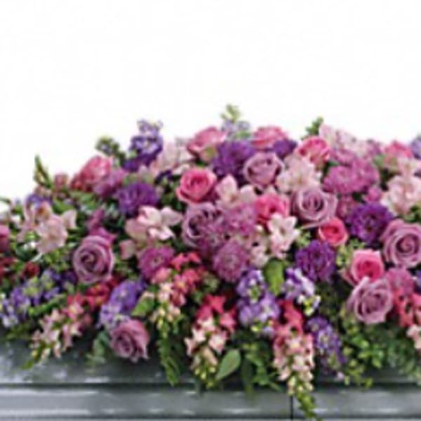 Large pink and purple floral casket spray on a gray casket
