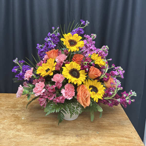 Mixed bouquet with sunflowers, orange roses, and pink carnations in a white vase