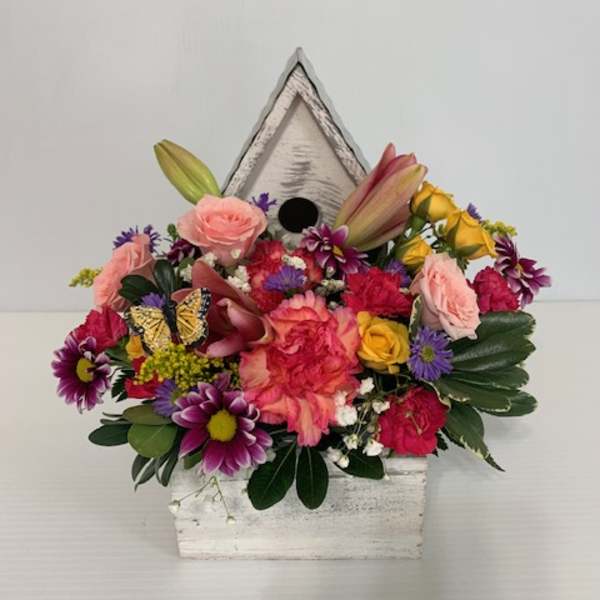 Mixed bouquet in a white birdhouse container with a butterfly accent