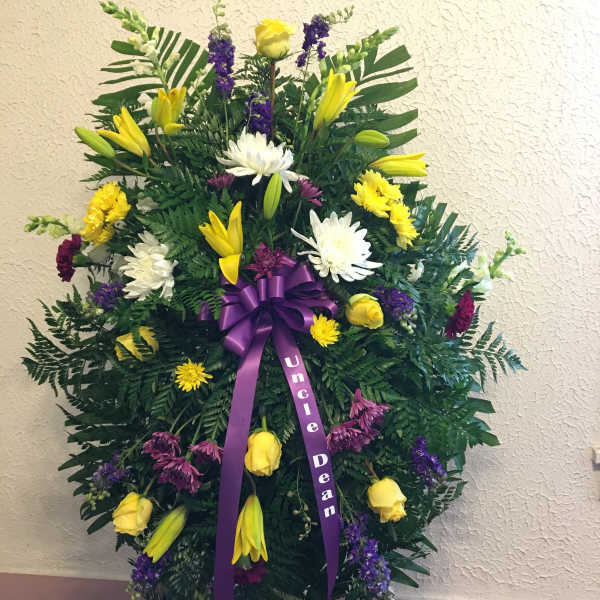 Standing funeral spray with yellow and white flowers and a purple ribbon