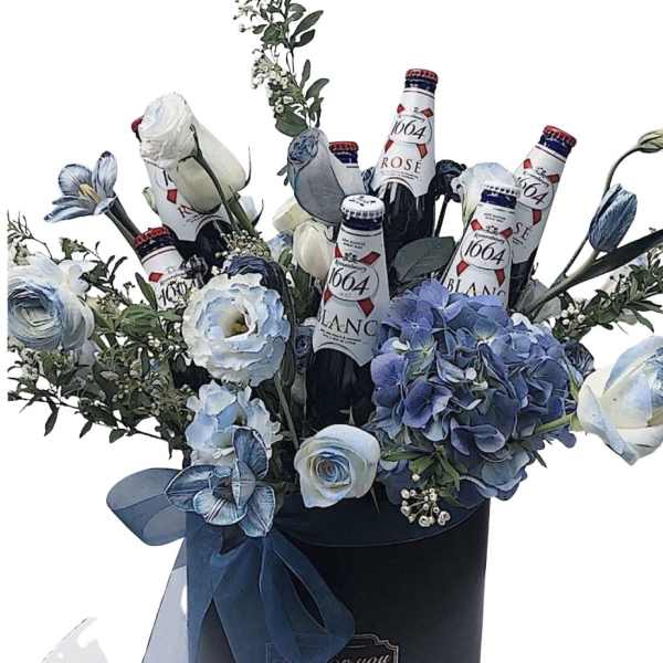 Blue and white flowers arranged with beer bottles in a black hatbox.