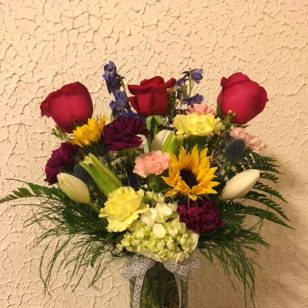 Mixed bouquet of roses, sunflowers, and carnations in a glass vase