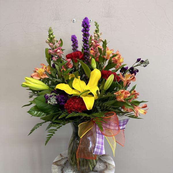 Mixed bouquet with yellow lilies, red carnations, and purple flowers in a glass vase