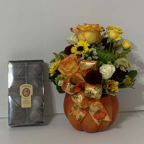 Pumpkin-shaped vase with yellow and orange roses and a chocolate box beside it