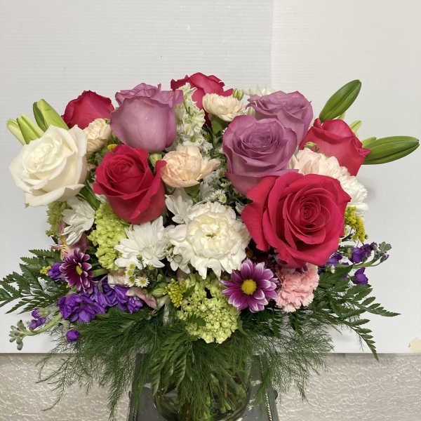 Mixed bouquet of roses, lilies, and daisies in a glass vase