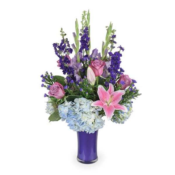 Purple and pink floral arrangement in a tall vase with lilies, roses, and hydrangeas