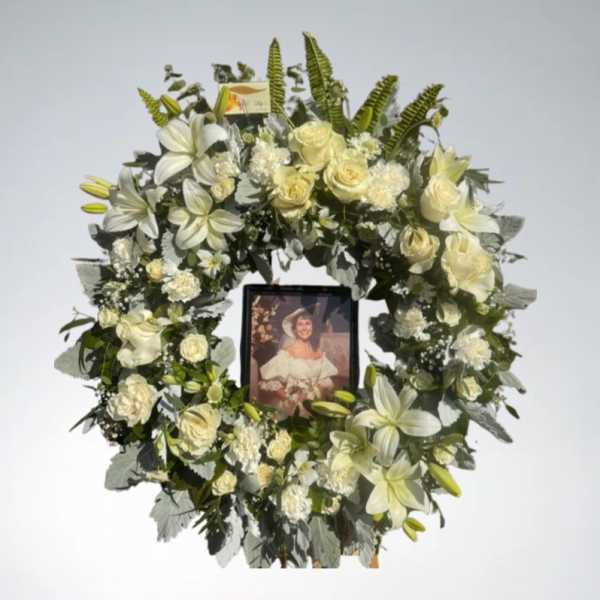 White floral funeral wreath with a framed photo in the center