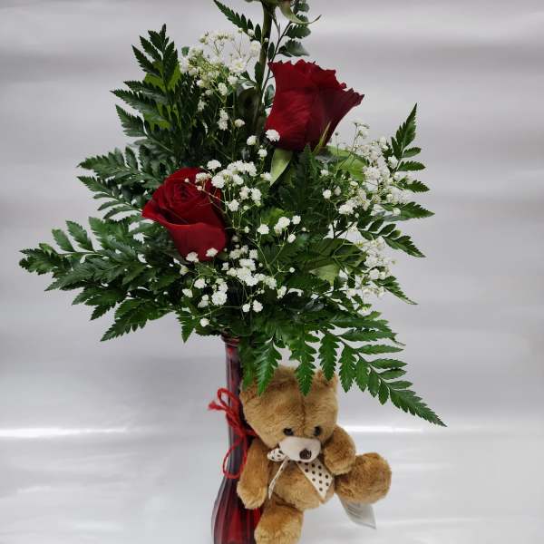 Red roses in a tall vase with baby's breath and a teddy bear