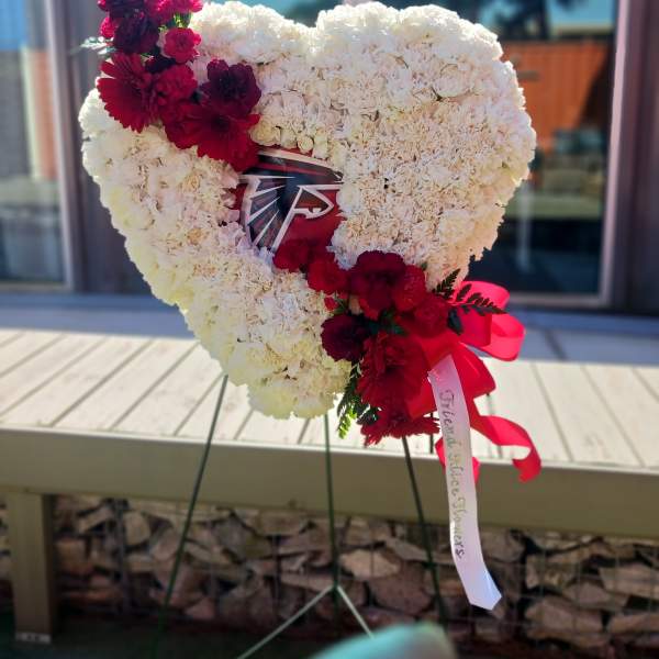 Heart-shaped white floral tribute with red flowers and ribbon