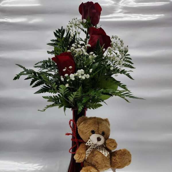 Red roses in a vase with a teddy bear attached