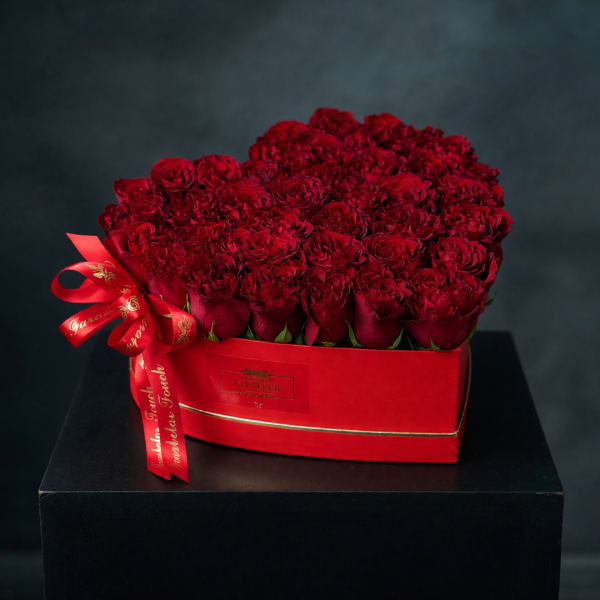 Red roses arranged in a red heart-shaped box with a ribbon bow