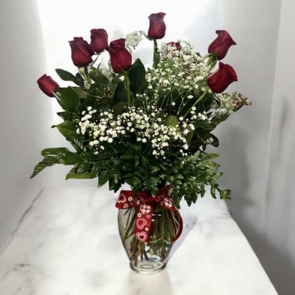 Red roses in a glass vase with baby's breath and a heart ribbon
