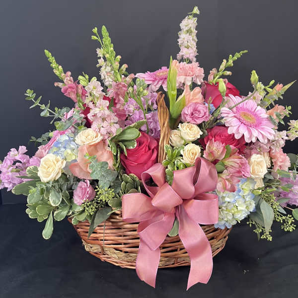 Basket arrangement of pink and cream flowers with a large pink ribbon