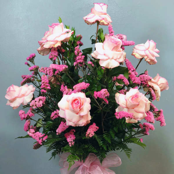 Tall arrangement of pink roses and pink filler flowers in a glass vase with a pink bow