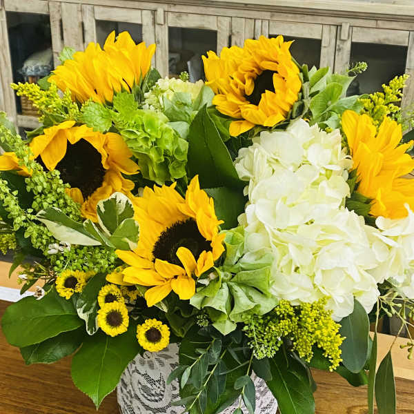 Sunflower and white hydrangea arrangement in a lace-wrapped vase