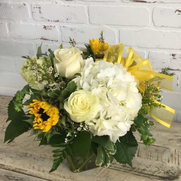 Bouquet of white roses, hydrangea, and sunflowers in a glass vase with yellow ribbon