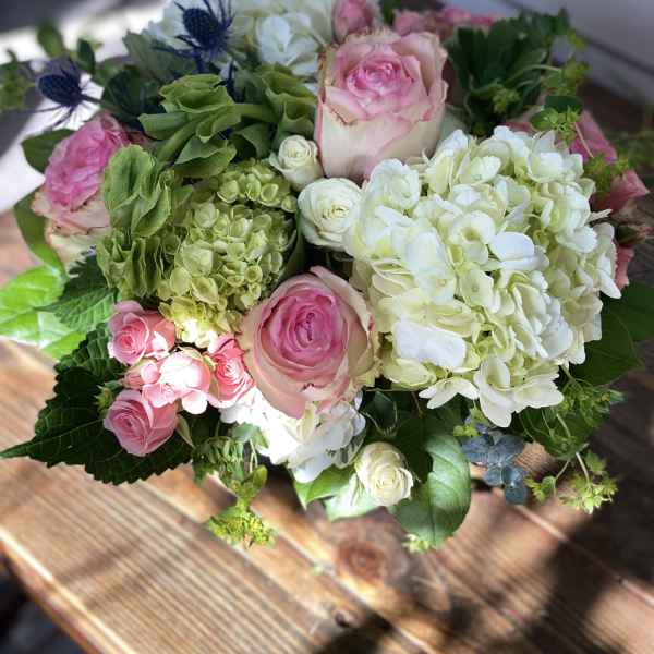 Round arrangement of pink roses with white and green hydrangeas in a low glass vase