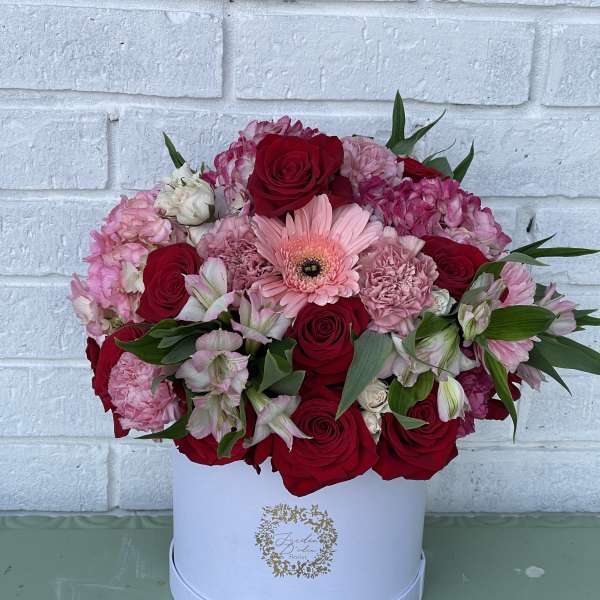 Pink and red flower arrangement in a white hat box