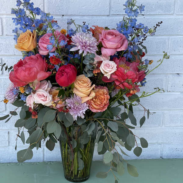 Mixed bouquet of roses, blue delphinium, and chrysanthemums in a glass vase