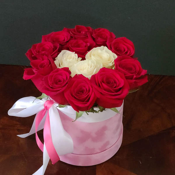 Red and white roses arranged in a pink round box with a ribbon