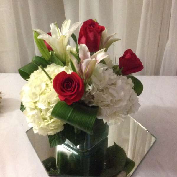Bouquet of red roses, white lilies, and white hydrangeas in a mirrored vase