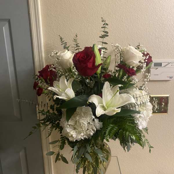 Tall bouquet of red and white roses with white lilies in a glass vase