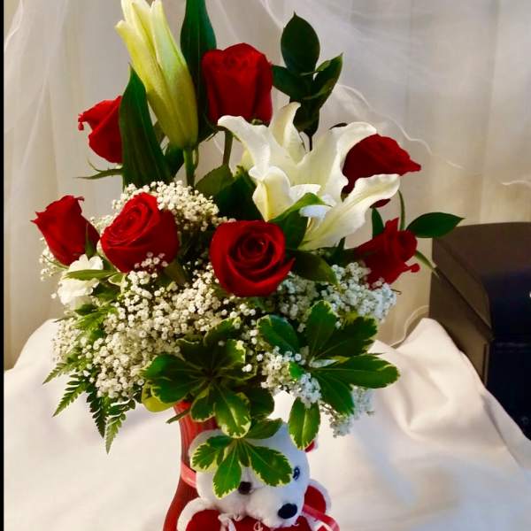 Red roses and white lilies in a red vase with a teddy bear