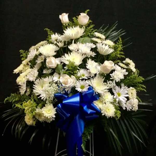 White floral standing spray with a blue ribbon on a metal easel