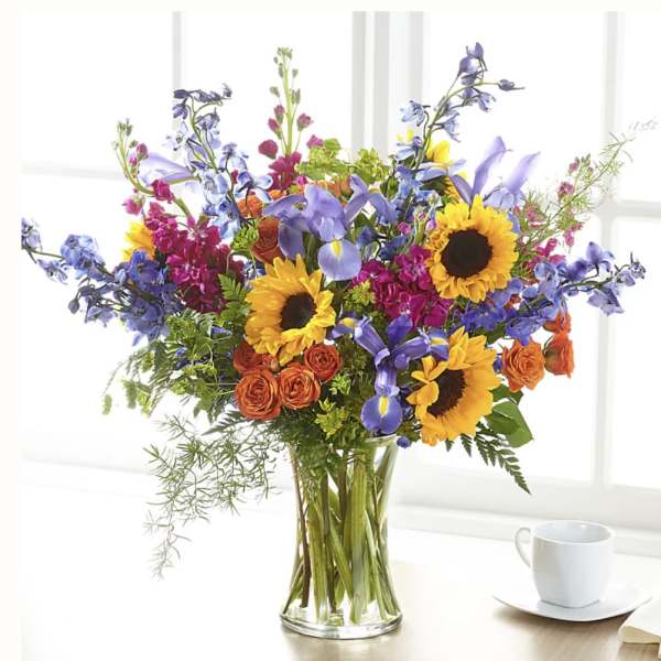 Colorful bouquet with sunflowers, purple irises, and orange roses in a glass vase
