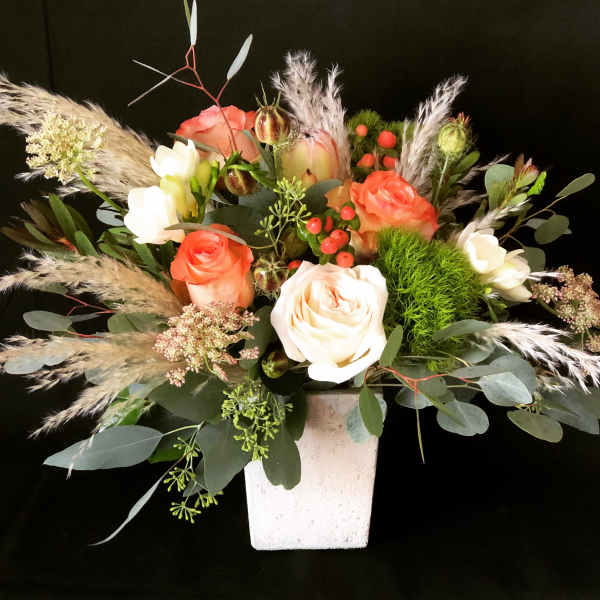 Mixed rose arrangement in a white square vase with airy grasses